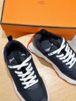 Sneakers navy di lusso con suola arancione e scatola elegante, stile moderno e raffinato.