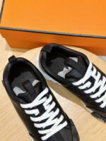 Scarpe da ginnastica nere con lacci bianchi, box arancione e design elegante su superficie in legno.
