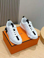 Sneakers bianchi moderne con dettagli neri su scatola arancione, stile urbano e di tendenza.
