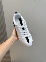 Sneaker bianca moderna con dettaglio nero, maneggiata a mano su sfondo minimalista.