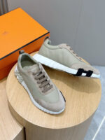 Sneakers beige eleganti con dettagli neri, suola comoda e design moderno su piedistallo in legno.