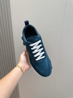 Sneaker navy blue con lacci bianchi, elegante e moderna, tenuta in mano su sfondo chiaro.