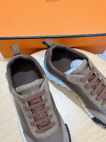 Sneakers moderne in pelle marrone con suola bianca e scatola arancione brillante.