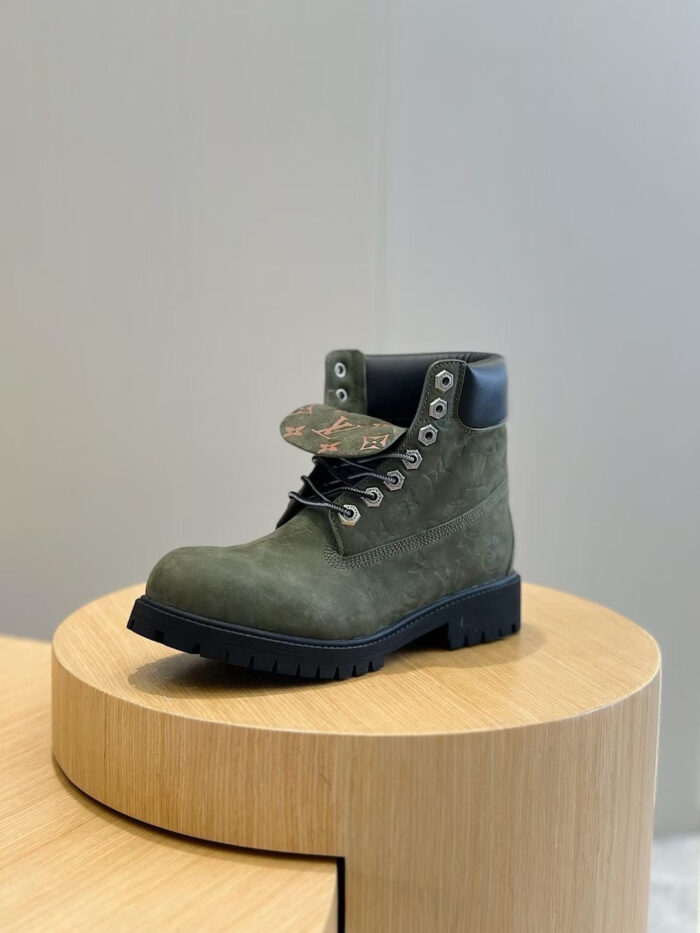 Stivale da esterno in camoscio verde con dettagli colorati e supporto in pelle, su piedistallo di legno.