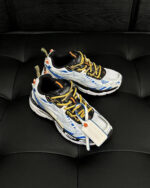 Sneakers sportive bianche con dettagli blu, arancioni e lacci gialli, comode e di tendenza.