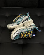 Sneakers sportive teal, bianco e giallo su superficie in pelle nera, ideali per attività e relax.