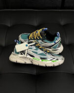 Sneakers colorate moderne con suola robusta, dettagli riflettenti e laccetti gialli e neri.