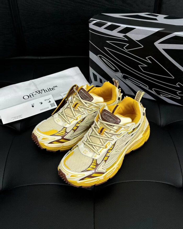 Sneakers Off-White beige e giallo su superficie nera con scatola geometrica moderna.