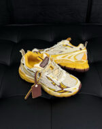 Sneakers beige e gialle moderne, sportive e alla moda su superficie nera tapizzata.