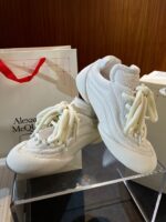 Sneakers Alexander McQueen bianche di design sportivo su sfondo in legno elegante.