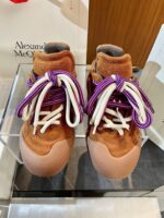 Sneakers alla moda con lacci viola e tomaia in suede terracotta su supporto di vetro.