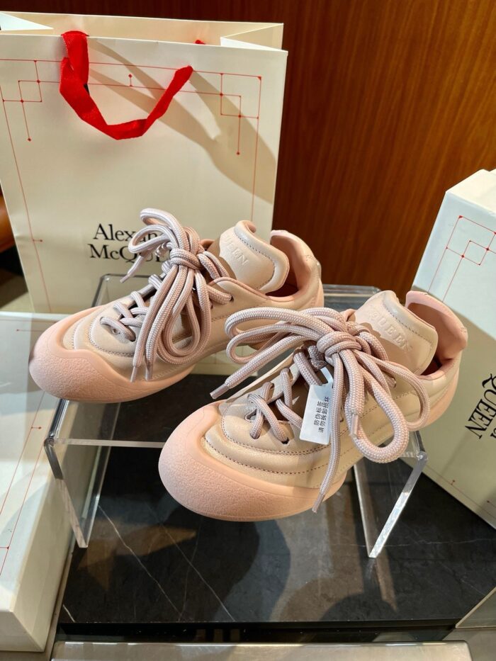 Sneakers rosa pastello di lusso Alexander McQueen su supporto di vetro in boutique elegante.