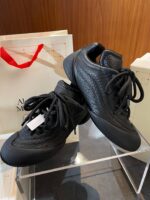 Scarpe sportive nere di design moderno, su supporto trasparente con dettaglio di confezione elegante.