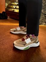 Scarpe sneakers beige e viola con pantaloni neri in ambiente caldo e raffinato.