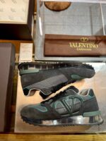 Sneakers Valentino Garavani di lusso con dettagli eleganti e accenti colorati, presentate su superficie trasparente.