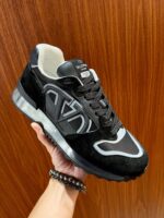 Scarpa sneaker nera con dettagli grigi, logo, suola trasparente e design elegante e confortevole.