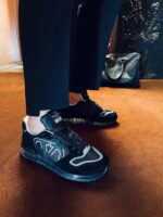 Scarpe sneakers nere con pantaloni su misura, sfondo caldo e elegante atmosfera moderna.