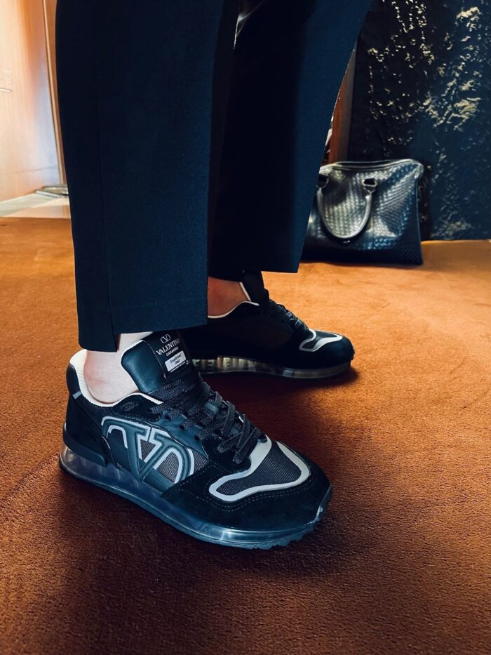 Scarpe sneakers nere con pantaloni su misura, sfondo caldo e elegante atmosfera moderna.