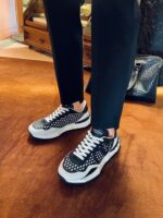 Sneakers nere moderne con dettagli bianchi, pantaloni slim e ambiente elegante, stile casual-chic.