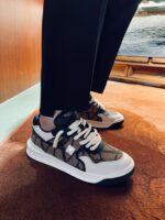 Sneaker beige e marrone su tappeto arancione con pantaloni neri eleganti, stile moderno e sofisticato.