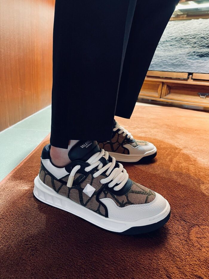 Sneaker beige e marrone su tappeto arancione con pantaloni neri eleganti, stile moderno e sofisticato.