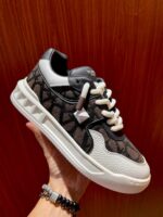 Sneaker moderna nera con dettagli metallici, lacci crema e suola robusta in stile streetwear.