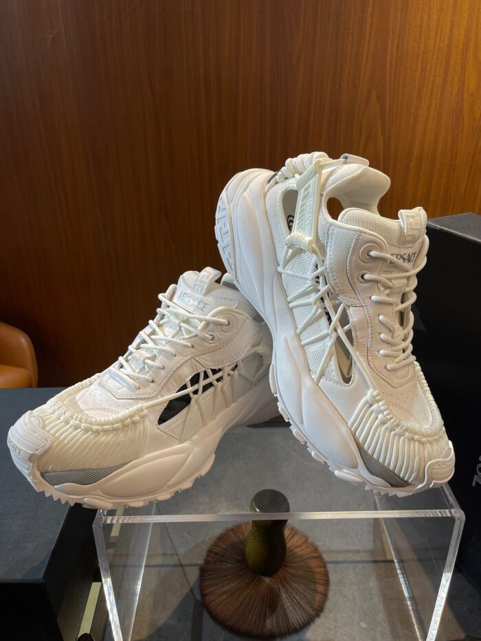 Sneaker bianche moderne con suola spessa e dettagli di design innovative su supporto trasparente.
