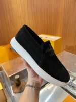 Scarpa slip-on in suede nero con suola bianca e dettaglio dorato, stile minimal e elegante.