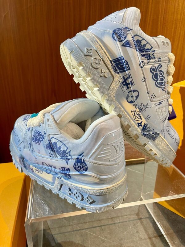 Sneakers artistiche blu e bianco su stand trasparente con design originale e stile moderno.