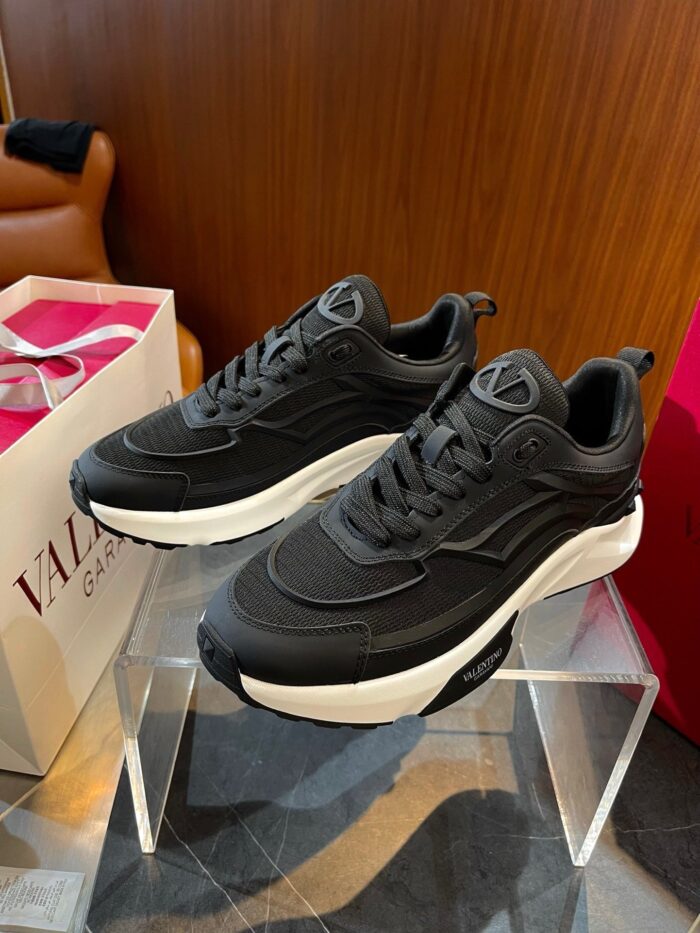 Sneakers moderne nere e bianche su supporto trasparente con dettagli di design eleganti.