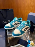 Sneakers Dior turquoise e bianco su pedana, packaging di lusso in ambiente elegante.