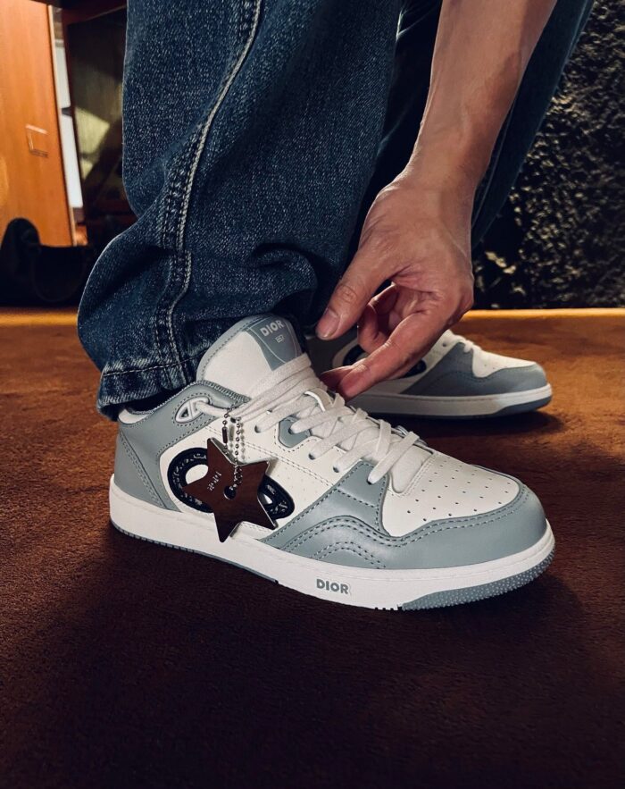 Sneakers bianche con logo stella, jeans scuri, gesto di allacciare le scarpe in soggiorno.