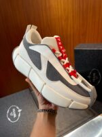 Sneaker moderna bianca con dettagli grigi, lacci rossi e design chunky in stile streetwear.