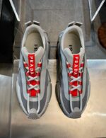 Sneakers Prada sportive in grigio con dettagli rossi e design moderno e elegante.