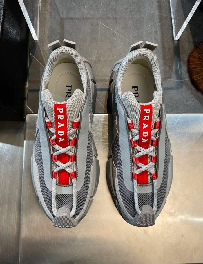 Sneakers Prada sportive in grigio con dettagli rossi e design moderno e elegante.