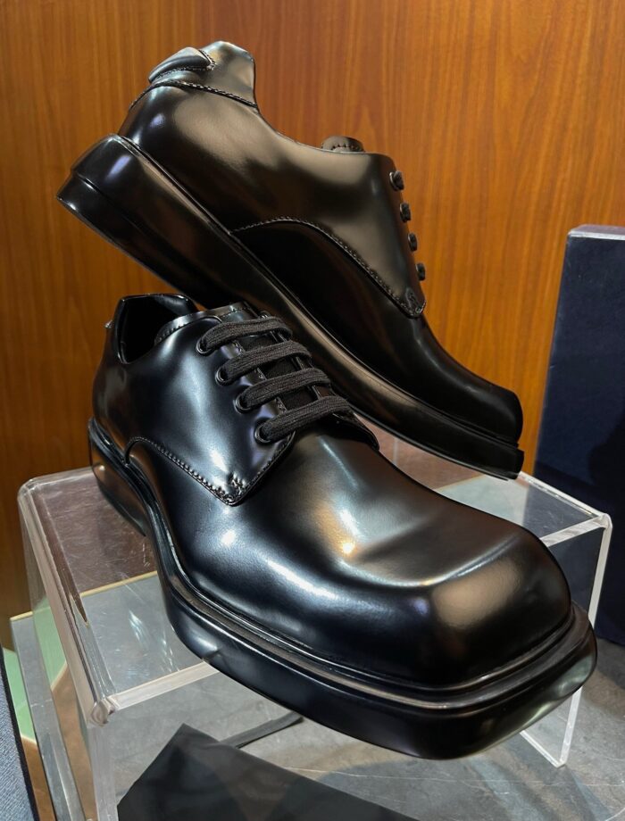 Scarpe eleganti in pelle nere su piedistallo di vetro, stile classico e moderno, perfette per occasioni formali.