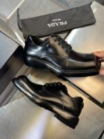Scarpe nere in pelle di lusso Prada con custodia elegante e riflesso su superficie raffinata.