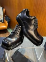 Scarpe eleganti in pelle nera su pedana di vetro, stile sofisticato e moderno.