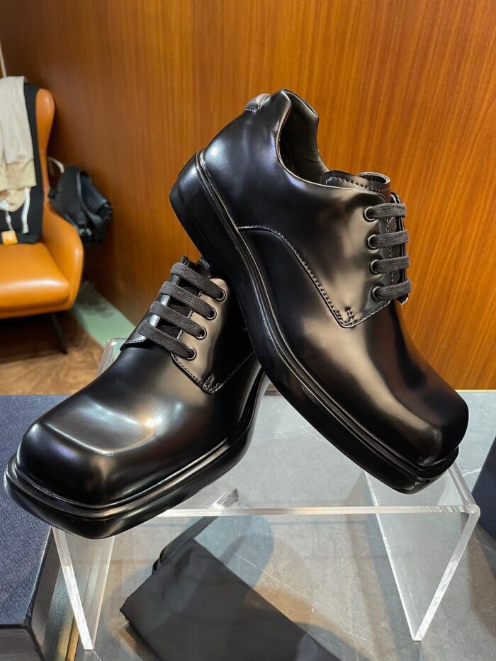 Scarpe eleganti in pelle nera su pedana di vetro, stile sofisticato e moderno.