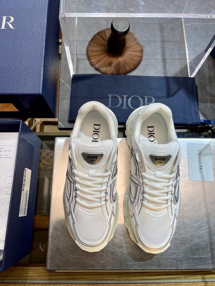 Sneakers di lusso bianche con dettagli moderni su superficie in vetro, brand di alta moda.