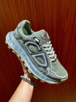 Sneaker moderna verde oliva con logo a contrasto, su sfondo in legno, vista dettagliata e stilosa.