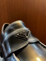 Scarpa Prada in pelle nera, elegante, con strap e logo triangolare in metallo.