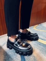 Scarpe nere di design con suola robusta e pantaloni slim eleganti in ambiente moderno.