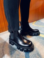 Stivaletti neri moderni con suola chunky, abbinati a pantaloni aderenti su tappeto astratto elegante.
