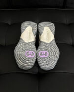 Sneakers moderne grigie con logo viola, dettagli di design e suola antiscivolo elegante.