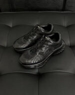 Scarpe sportive nere moderne con suola ondulata e design elegante su sfondo nero tufted.