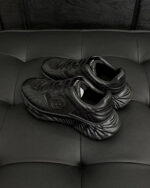 Sneakers nere in pelle lucida su divano rivestito in stile tufting elegante.