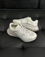 Sneakers bianche moderne con suola ondulata, dettagli in mesh e logo circolare elegante.