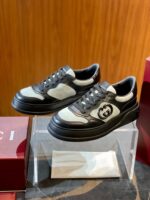 Sneakers di lusso nere con logo, suola chunky, presentate su base elegante con scatole rosse.