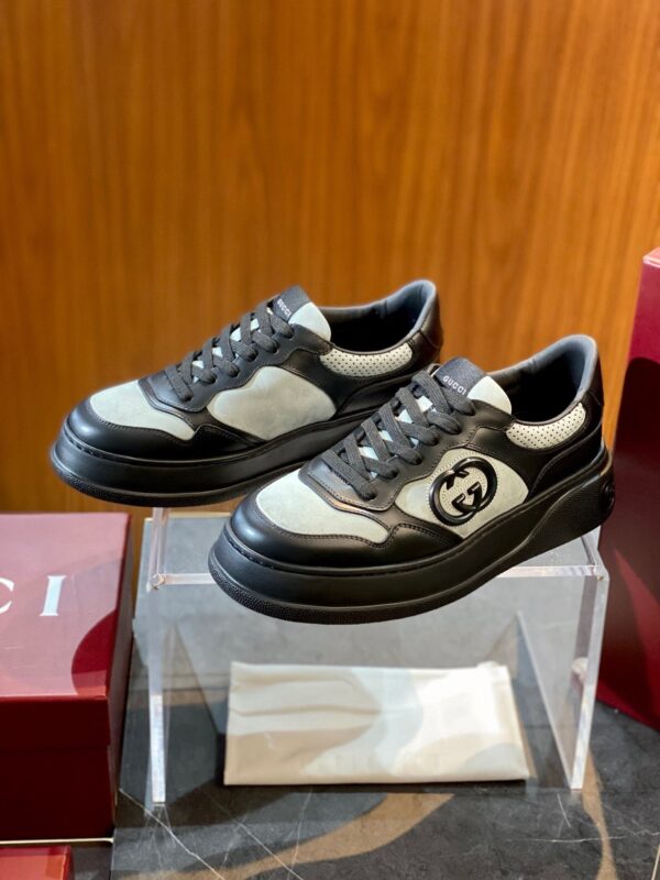 Sneakers di lusso nere con logo, suola chunky, presentate su base elegante con scatole rosse.